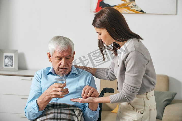 Young adult daughter giving pills to senior father while taking care of him after stroke