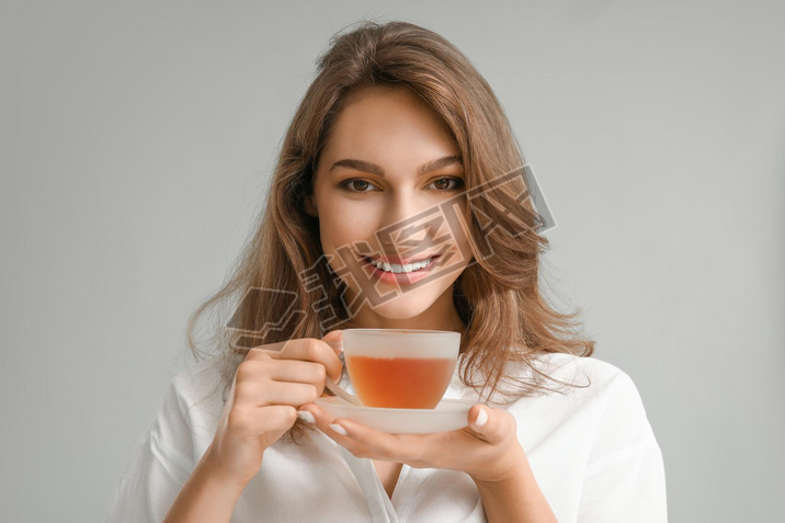 Beautiful young woman with cup of tea on grey background