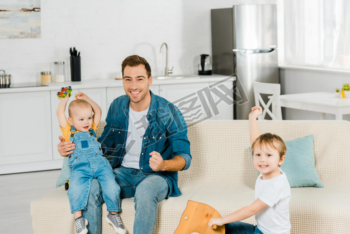 happy father looking at camera while spending time and playing with cheering preschooler and toddler