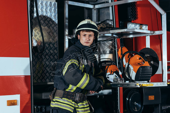 portrait of firefighter in helmet standing at truck at fire station