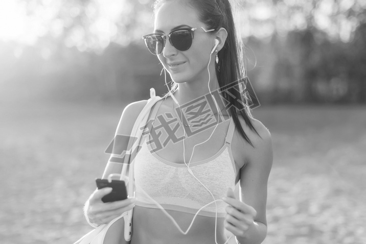 Black and white Athlete woman listening music looking at artphone after workout in nature outdoors