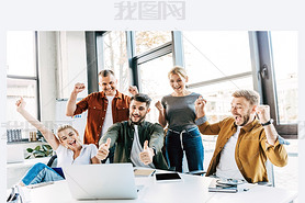 group of young successful entrepreneurs celebrating victory and showing thumbs up at office and look