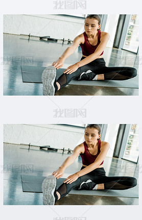 concentrated sportswoman sitting on mat and doing stretching exercise at gym