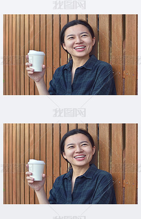 Smiling young lady standing at the wooden wall outdoors and holding a cup of coffee.