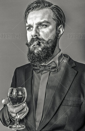 Portrait of a successful young man with retro look holding a glass of wine and oking a cigar over 