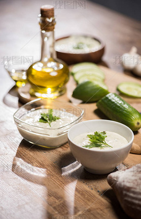 Tzatziki sauce in bowls with ingredients and olive oil on wooden table 