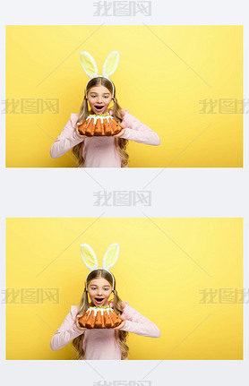 shocked kid with bunny ears holding easter cake isolated on yellow 