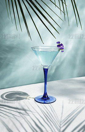 Cocktail blue colored on the table with sun shadows and reflection of water. On a blue background wi