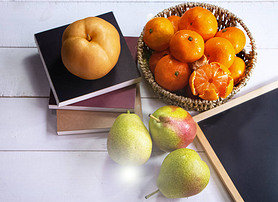 Group of orange fruit put in woven basket,beside blurred Chinese pear,on white timber board,blurry l