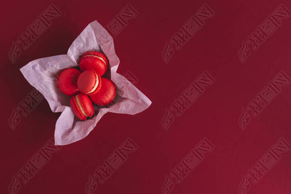 Red french macarons in a box on a dark red background.