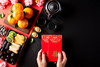 中国新年装饰品。 女性手拿着便盆或红包，橙色和金色的锭纹在黑色的石头背景上。 汉字