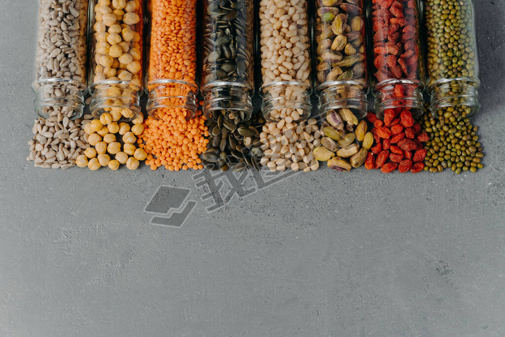 Vegetarian products full of protein spilled from glass containers on grey background with copy space