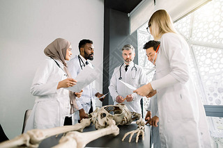 Team of young diverse doctors, students, scientists in white labcoats having discussion on the meeti