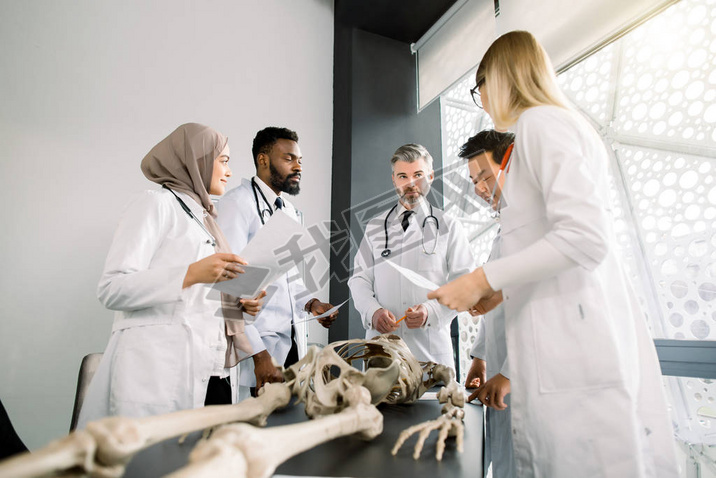 Team of young diverse doctors, students, scientists in white labcoats having discussion on the meeti