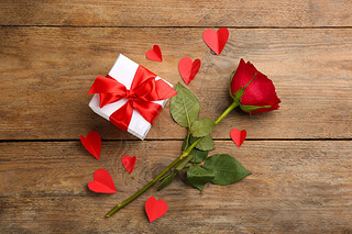 Beautiful gift box, paper hearts and rose on wooden table, flat lay. Valentine's Day celebration