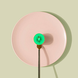 Neon green kiwi fruit on a fork against pastel pink plate. Unhealthy food minimal concept.