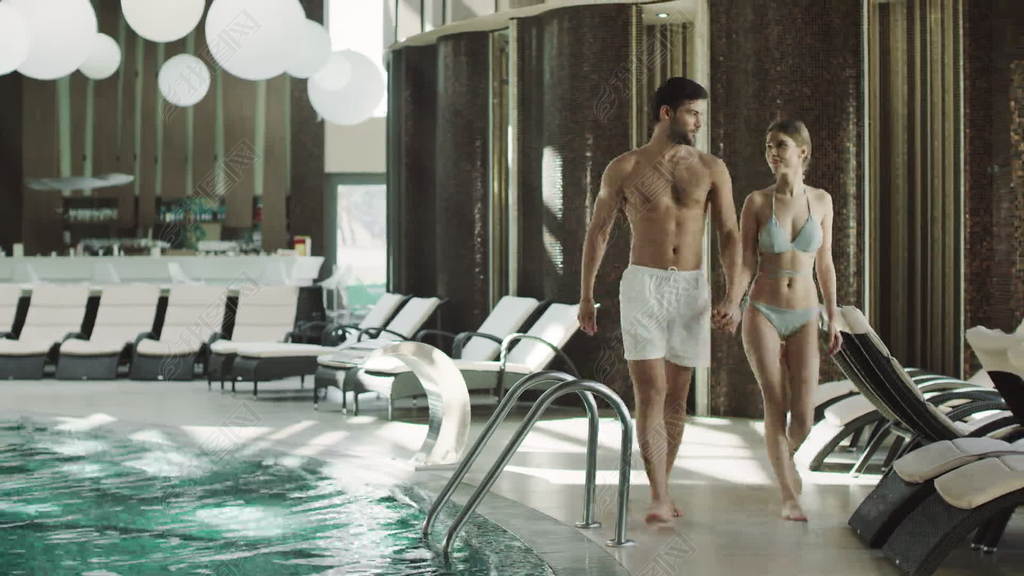 Smilingcouplewalkingindoorpoolatluxuryhotel.Holdinghandscouple.