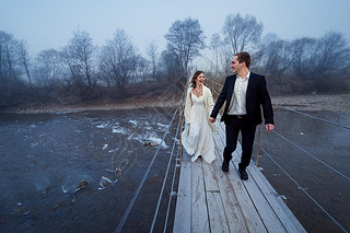 Happy wedding couple laughing and hing fun on the suspension bridge in mountains