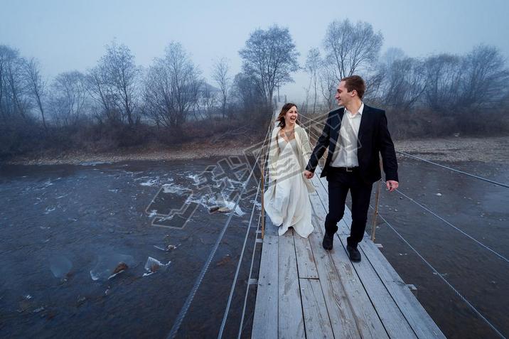 Happy wedding couple laughing and hing fun on the suspension bridge in mountains