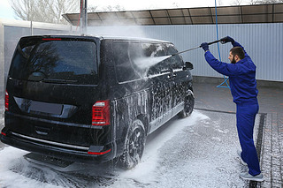Worker cleaning automobile with high pressure water jet at car w