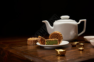 传统美味的中国月饼, 茶壶和金锭在木桌上隔离在黑色