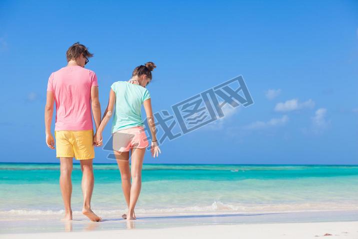 back view of happy romantic young couple walking on the beach