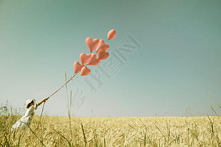 Young romantic girl with red heart balloons walking in a field o