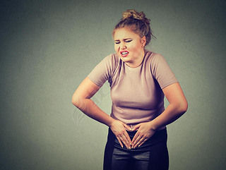 Young woman hands on stomach hing bad aches pain. Food poisoning, influenza, cramps.