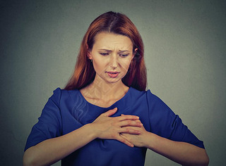 young woman with breast pain touching chest isolated on gray wall background