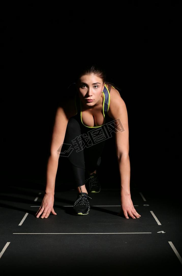 Athletic woman in position ready to run on black background.