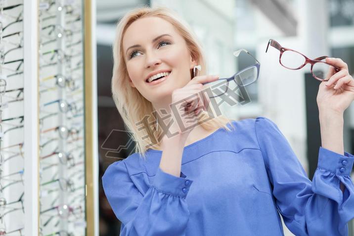 Pretty blond girl is choosing glasses in store