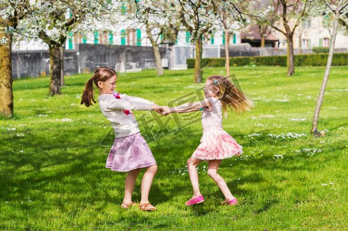 Two little girls playing in spring garden on a nice sunny warm day, wearing skirts