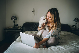 young woman indoors at home sitting bed using laptop computer holding dog - social network, wifi tec