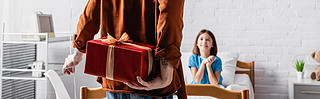 back view of man holding gift box near joyful daughter in hospital bed on blurred background, banner