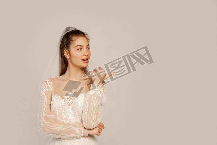 young bride looking away and pointing with thumb isolated on grey 