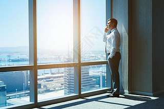 Mature and cnofident business executive looking looking out of large windows at a view of the city b