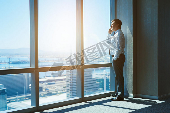 Mature and cnofident business executive looking looking out of large windows at a view of the city b