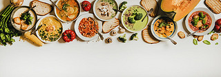 Flat-lay of creamy homemade soup in plates with bread slices over white plain table background, top