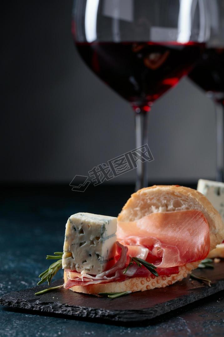 Sandwich with prosciutto, blue cheese and rosemary on a dark background. Delicious snack and glasses