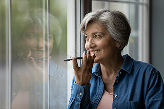 Happy middle aged elderly woman recording audio message.