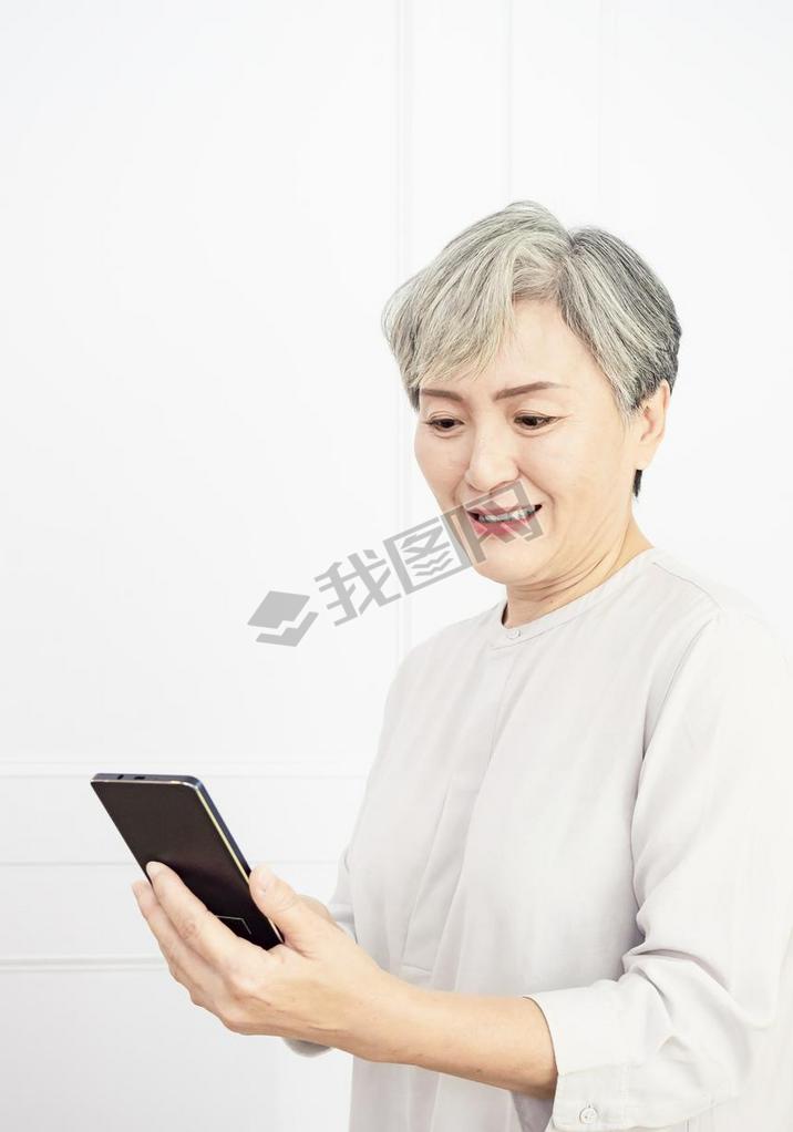 Happy mature senior asian woman holding artphone using mobile online apps.
