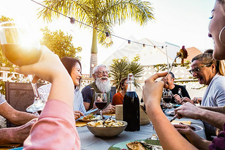 Happy family doing a dinner during sunset time outdoor - Group of diverse friends hing fun dining