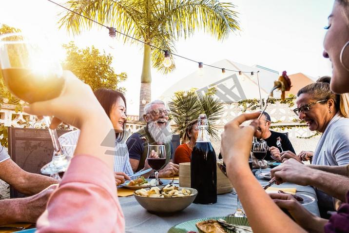 Happy family doing a dinner during sunset time outdoor - Group of diverse friends hing fun dining 