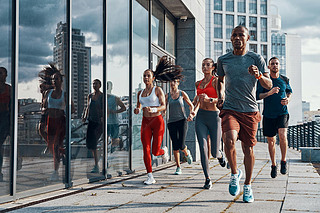 Group of people in sports clothing jogging outdoors in city at modern building with glass windows