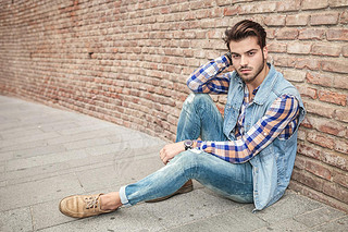 handsome man resting on the sidewalk, leaning against a wall