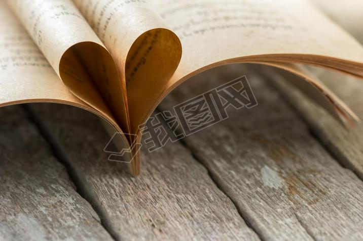 Heart shape from opened book pages on wooden background.