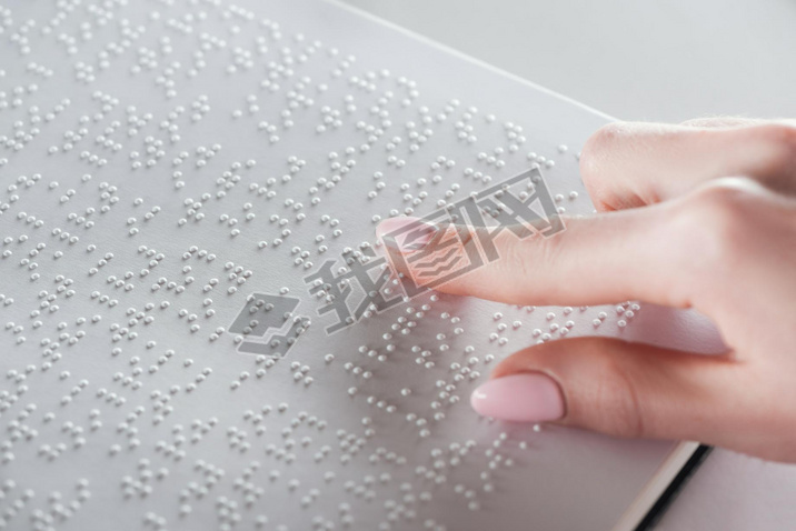 partial view of young woman reading braille text on white paper