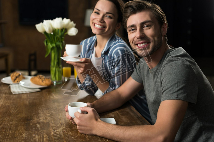 Smiling wife and husband drinking coffee in kitchen