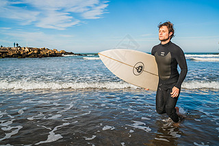 Surfer leing the water with surfboard under his arm.