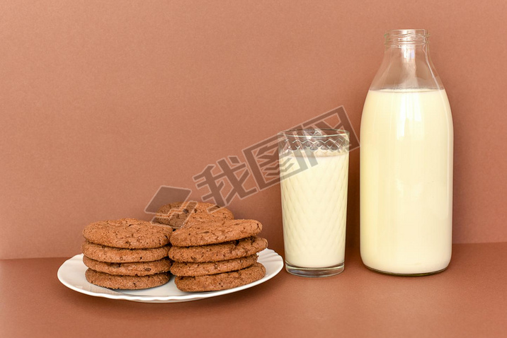 Milk in glass bottle and transparent glass and cookies on white plate 